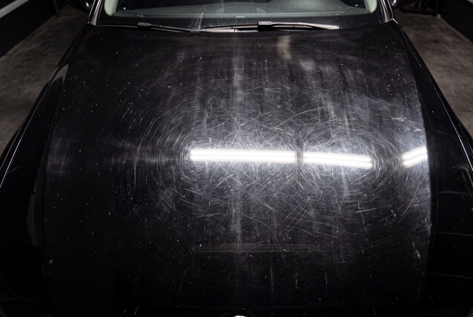 Black hood covered in swirl marks before paint correction